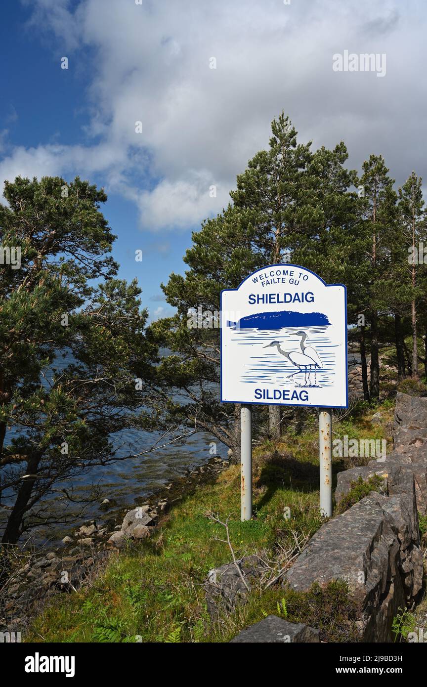 Welcome to Shieldaig sign with background of pine trees and water. Blue sky and clouds, sunny day. No people. Stock Photo
