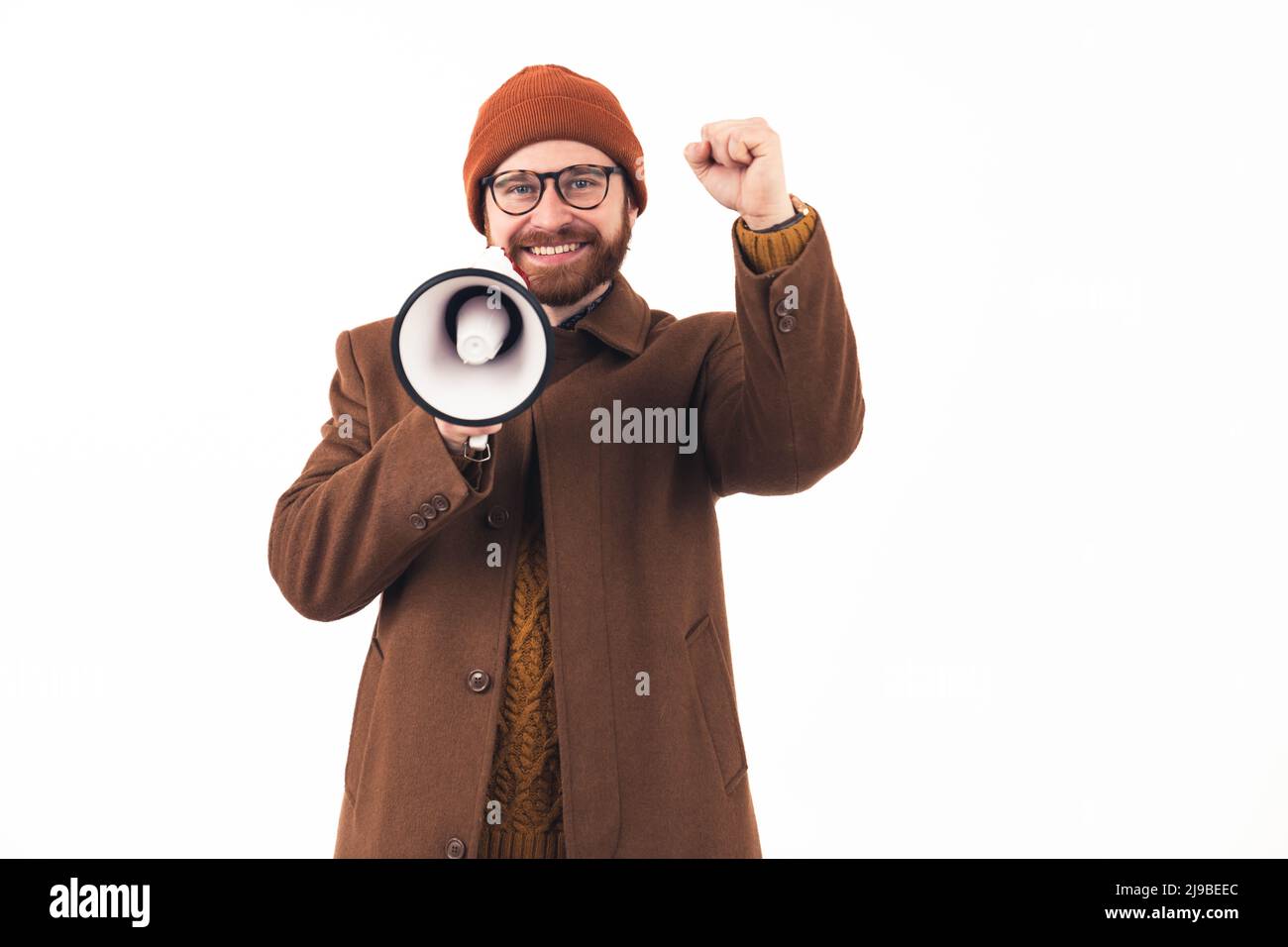 It's time for sales. Studio shot of a hipster millennial man in brown autumn outwear holding loudspeaker and throwing his fist in the air over white background. High quality photo Stock Photo
