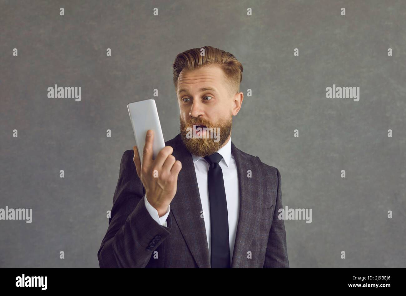 Businessman in suit looking at mobile phone with happy surprised face expression Stock Photo