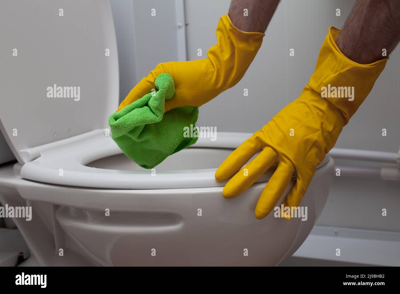Close up photo of hands wearing yellow gloves cleaning a white WC