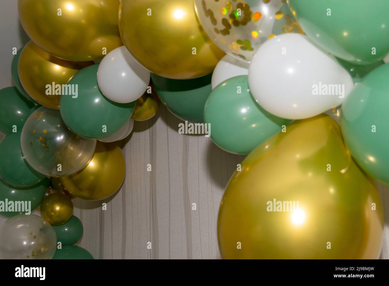 Golden Green and white balloons hanging on a wall, party or events decorations. Birthday partying. Stock Photo