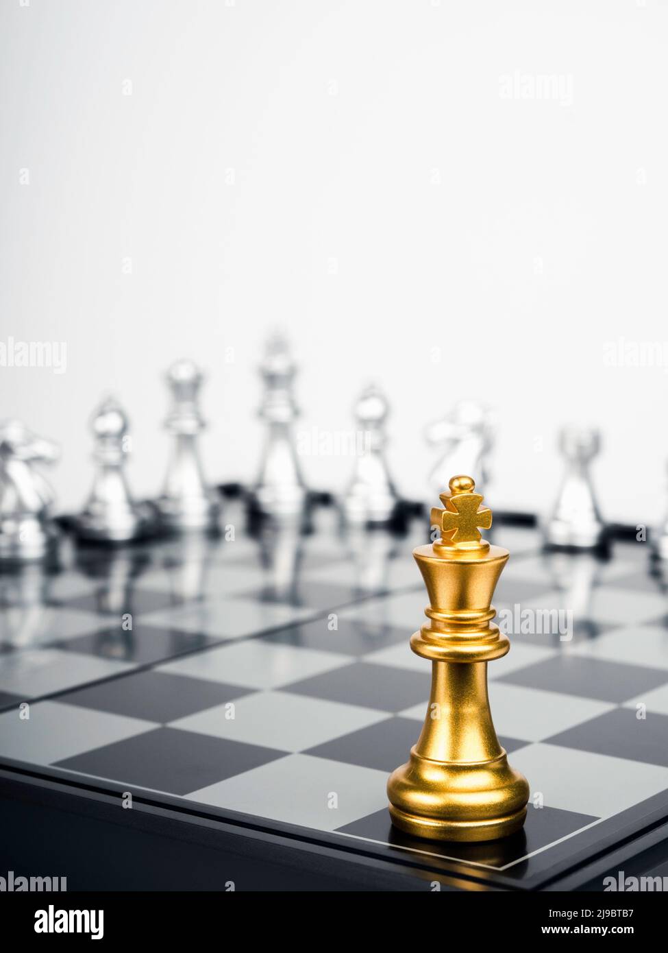 The Golden king chess piece standing on chessboard corner in front of silver chess pieces on white background, vertical. Leadership, fighter, competit Stock Photo