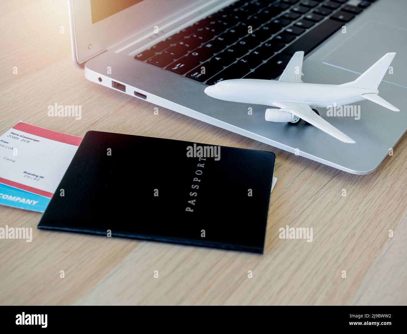 white airplane toy on the laptop computer with passport black cover and flight ticket on wooden desk. Online ticket booking for travel concept. Stock Photo