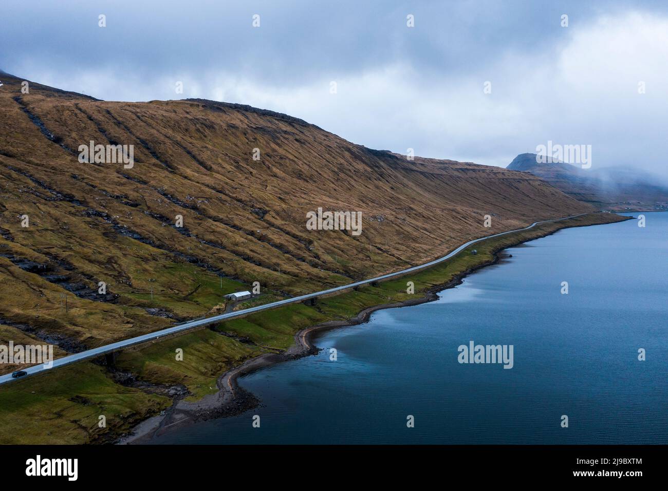 A virtually empty road in the Faroe Islands surrounded only by grassy mountains and the sea. Stock Photo