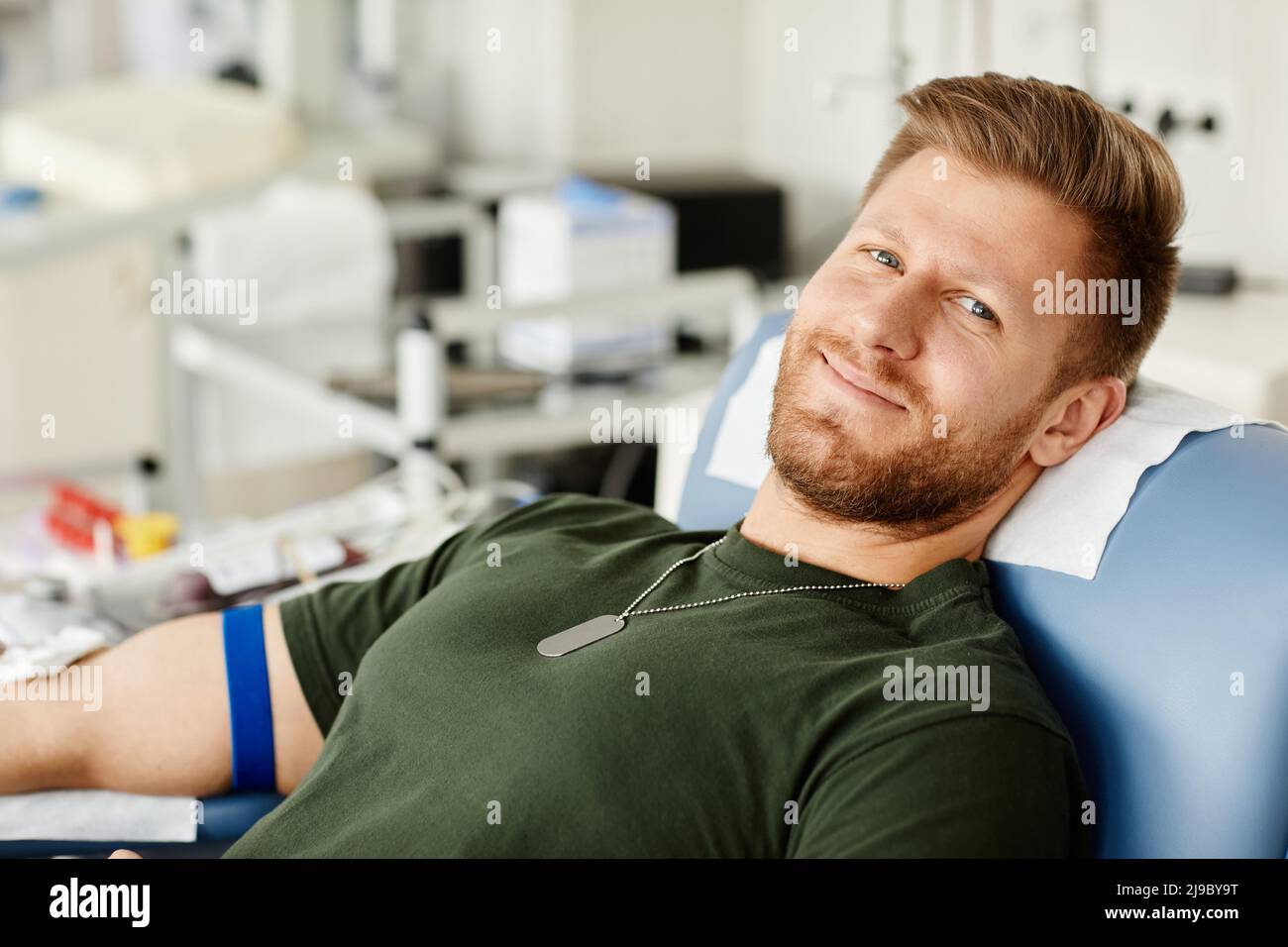 Portrait of smiling soldier giving blood while laying in chair at blood donation center and looking at camera Stock Photo