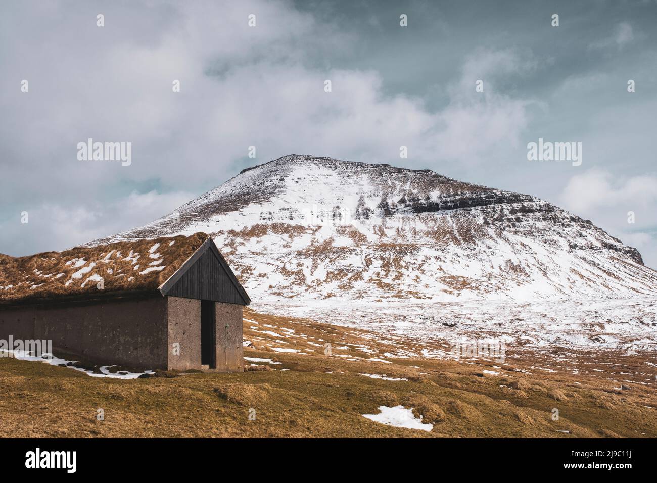 The traditional stone and natural roof of this farm building blend in with the colours of the majestic snowy mountain behind. Stock Photo