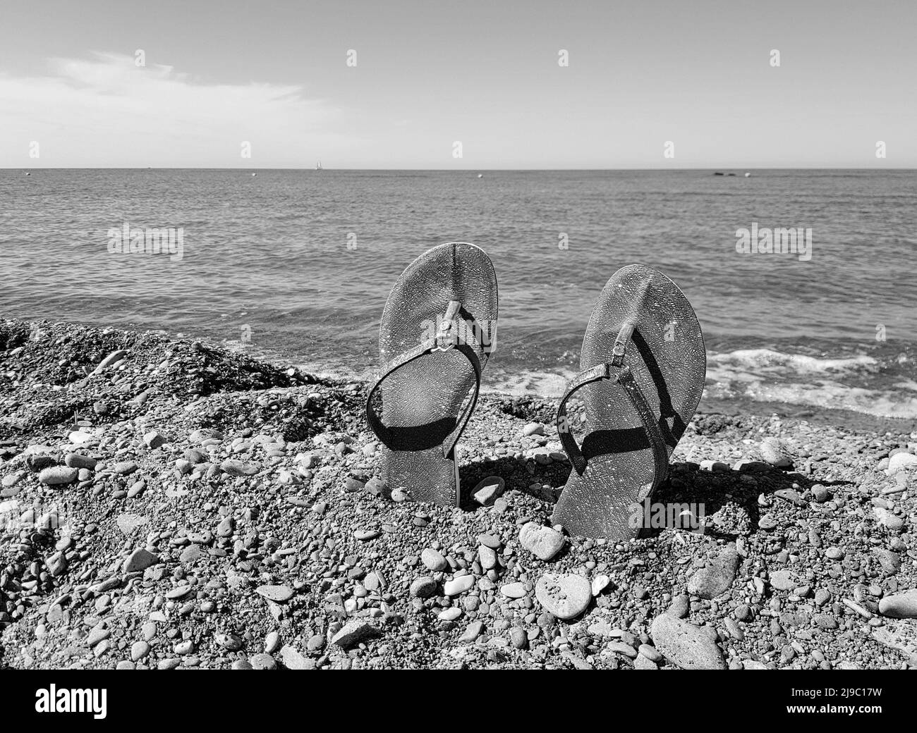 Black and white photo, women's beach shoes standing on a pebble against ...