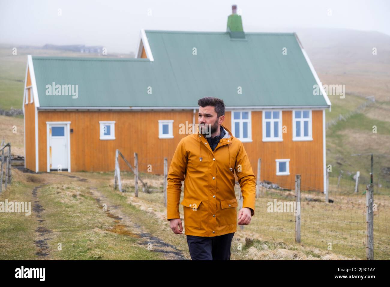 This delightful cottage and the man's matching raincoat stand out against the white-grey sky and sea. Stock Photo