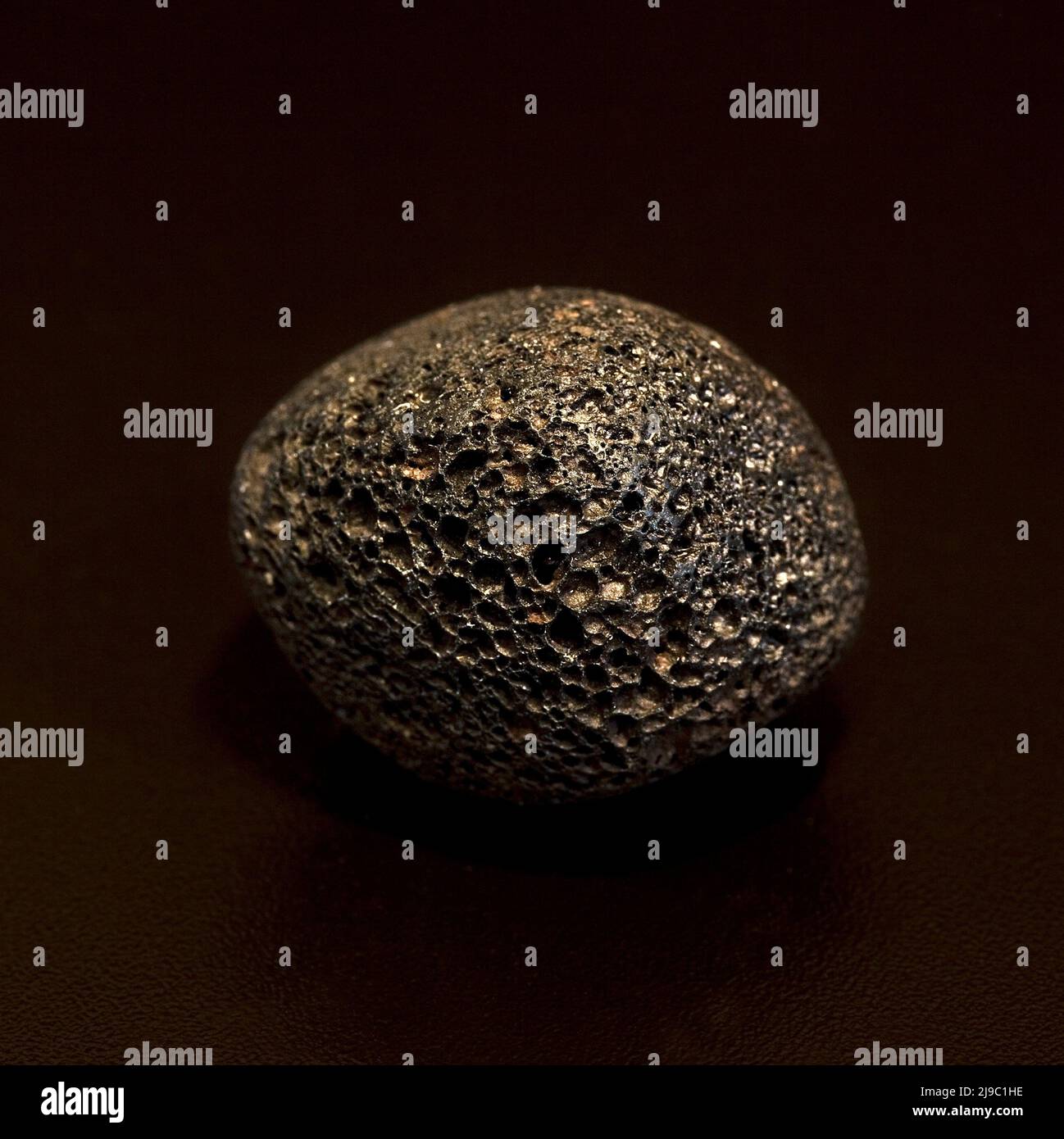 Macro close up colour photograph of a tumbled 'Lava Rock' a semi precious crystal gemstone used in crystal healing therapy Stock Photo