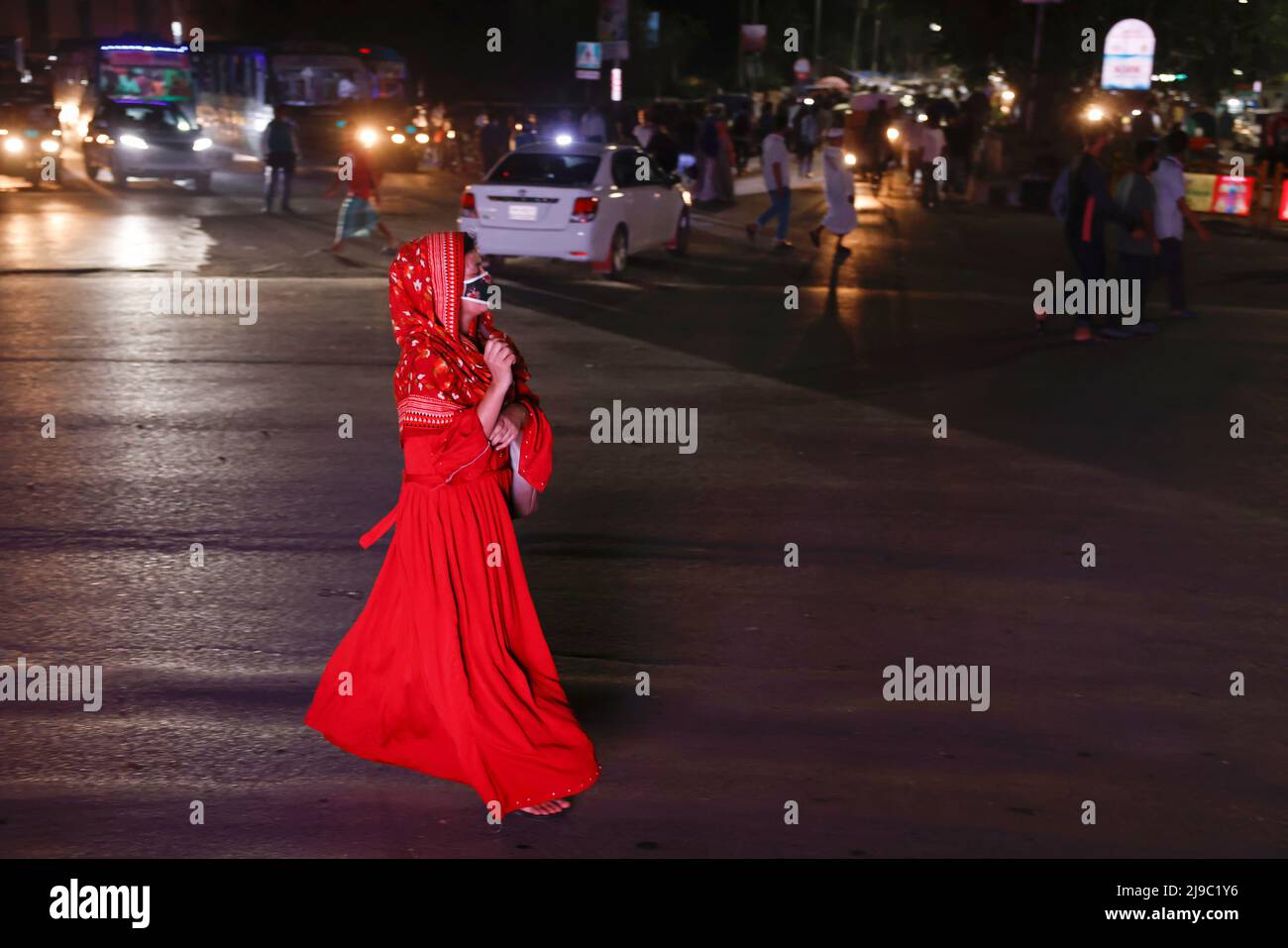 A woman wearing a red dress, crosses a road at night in Dhaka, Bangladesh, May 22, 2022. REUTERS/Mohammad Ponir Hossain Stock Photo