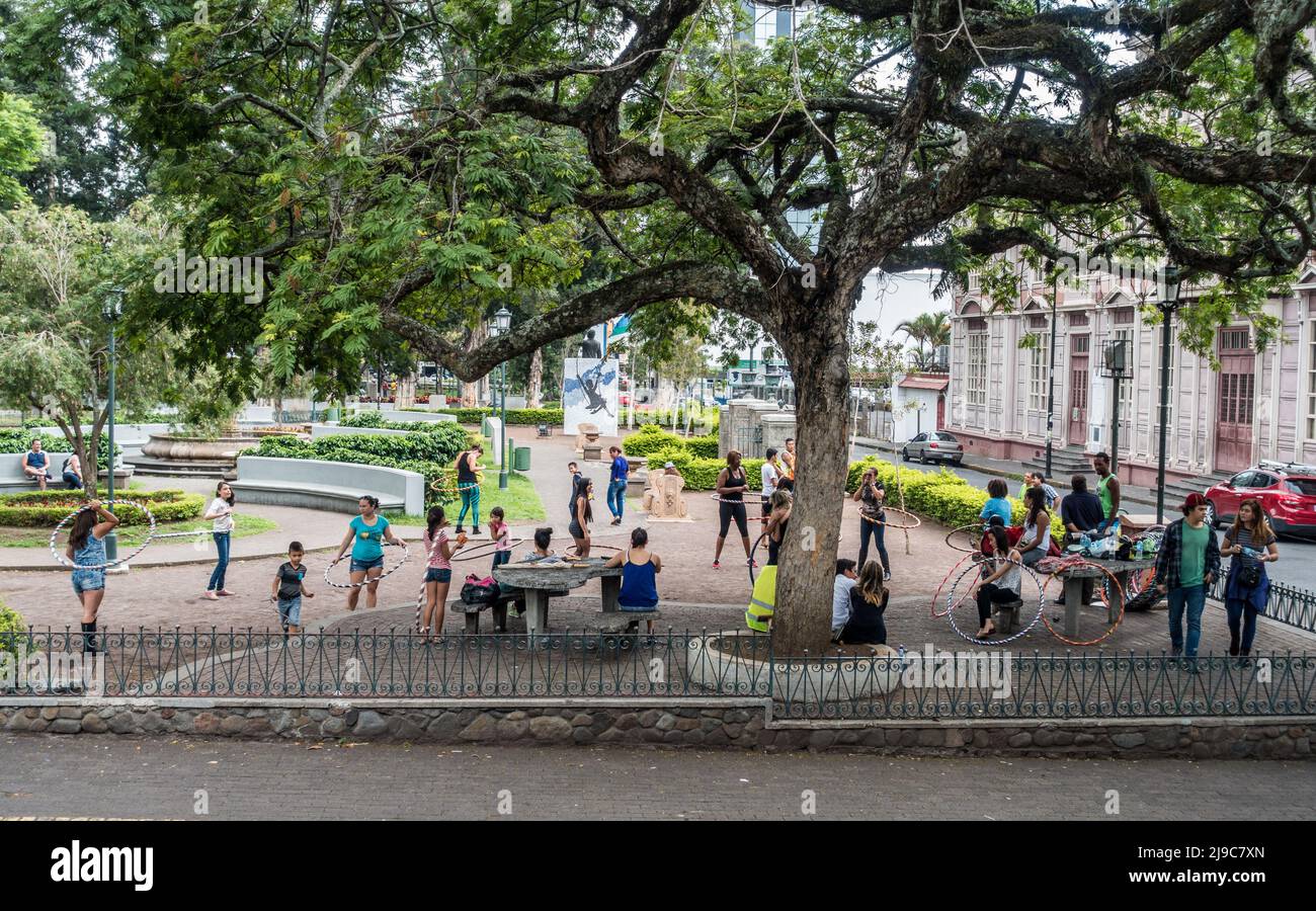 Group  of people exercising with hula hoops under a large tree in a park in San José, Costa Rica. Stock Photo