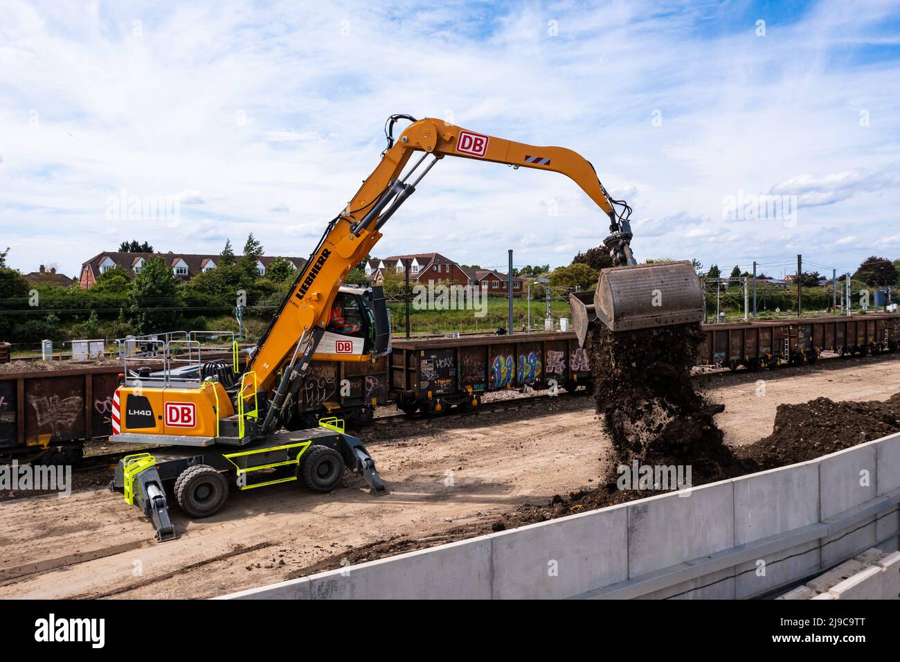 PETERBOROUGH, UK - MAY 17, 2022.  A heavy plant digger machine unloading spoil and earth from the wagons of a freight train after railroad engineering Stock Photo