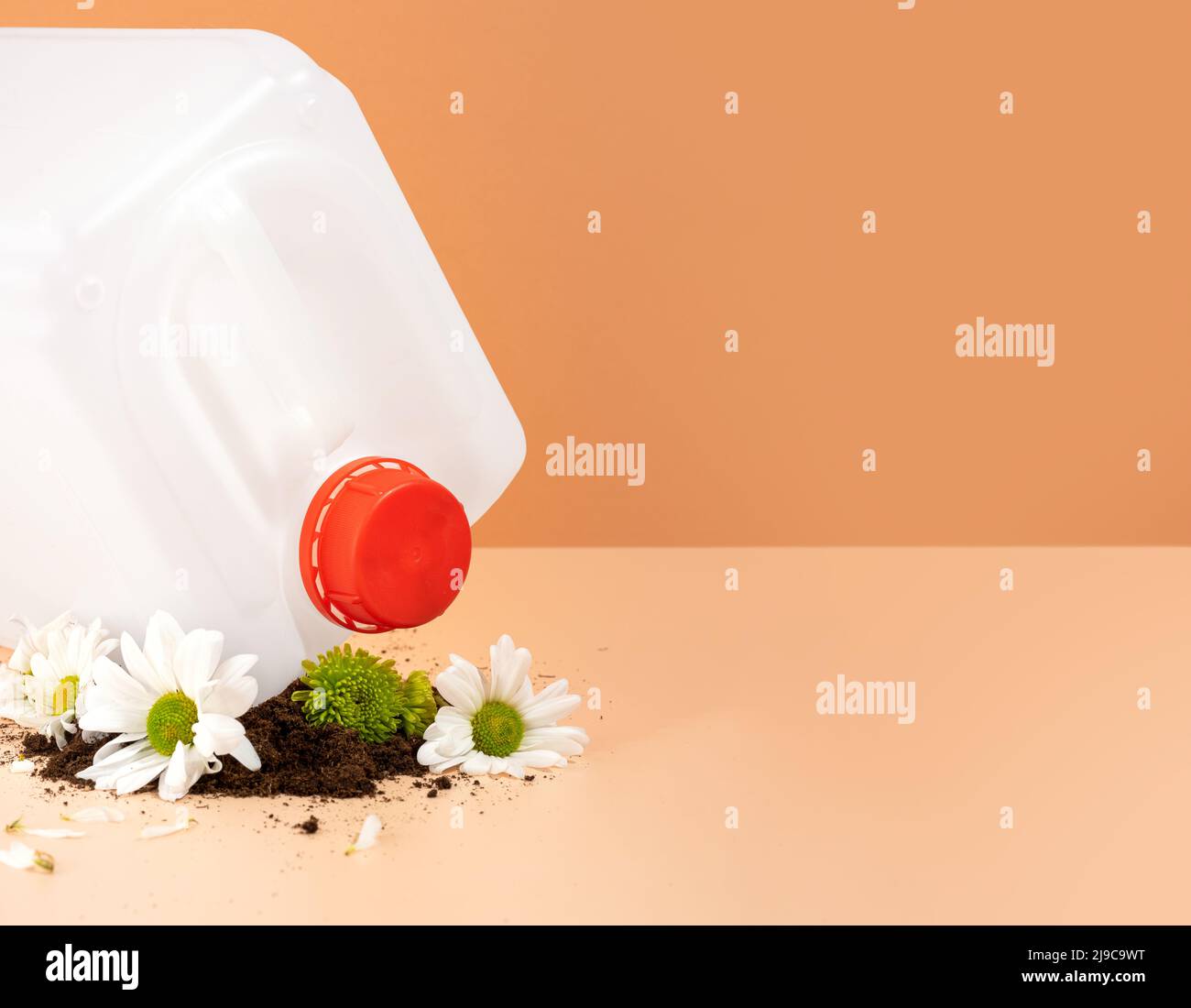 Negative impact on nature. Plastic canister crushes beautiful flowers on an orange background. The concept of environmental damage. Stock Photo
