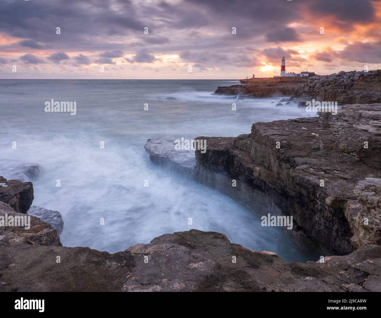 Looking across rocky ledges towards Portland Bill lighthouse in Dorset at sunset. Stock Photo