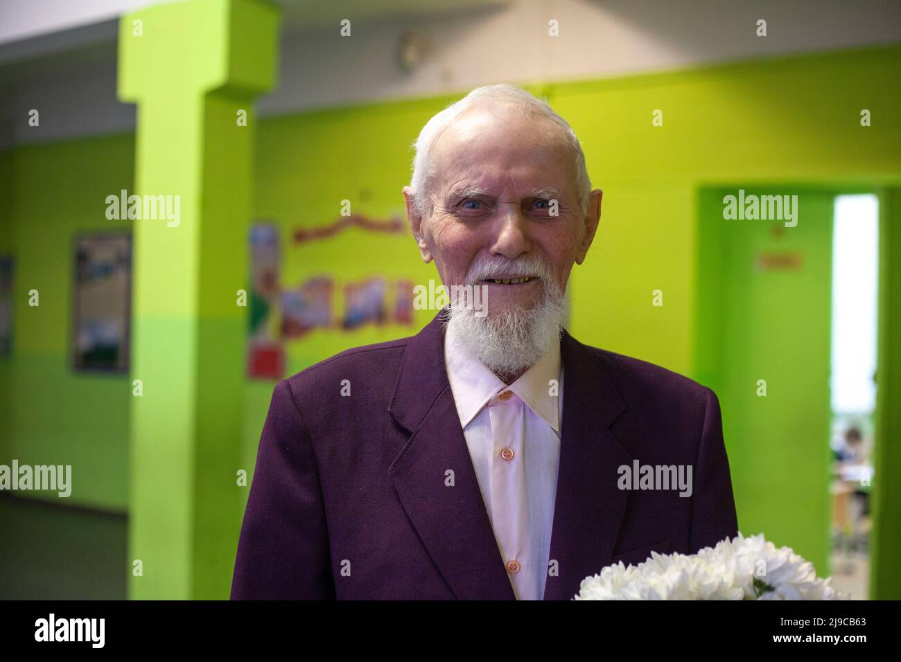 The old man holds flowers in his hand and smiles. A man who is 90 years