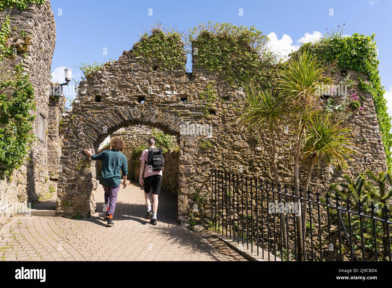 Two visitors to the harbour town of Tenby walking through the remains of Tenby Castle gateway on Castle Hill in May. Pembrokeshire, Wales Stock Photo