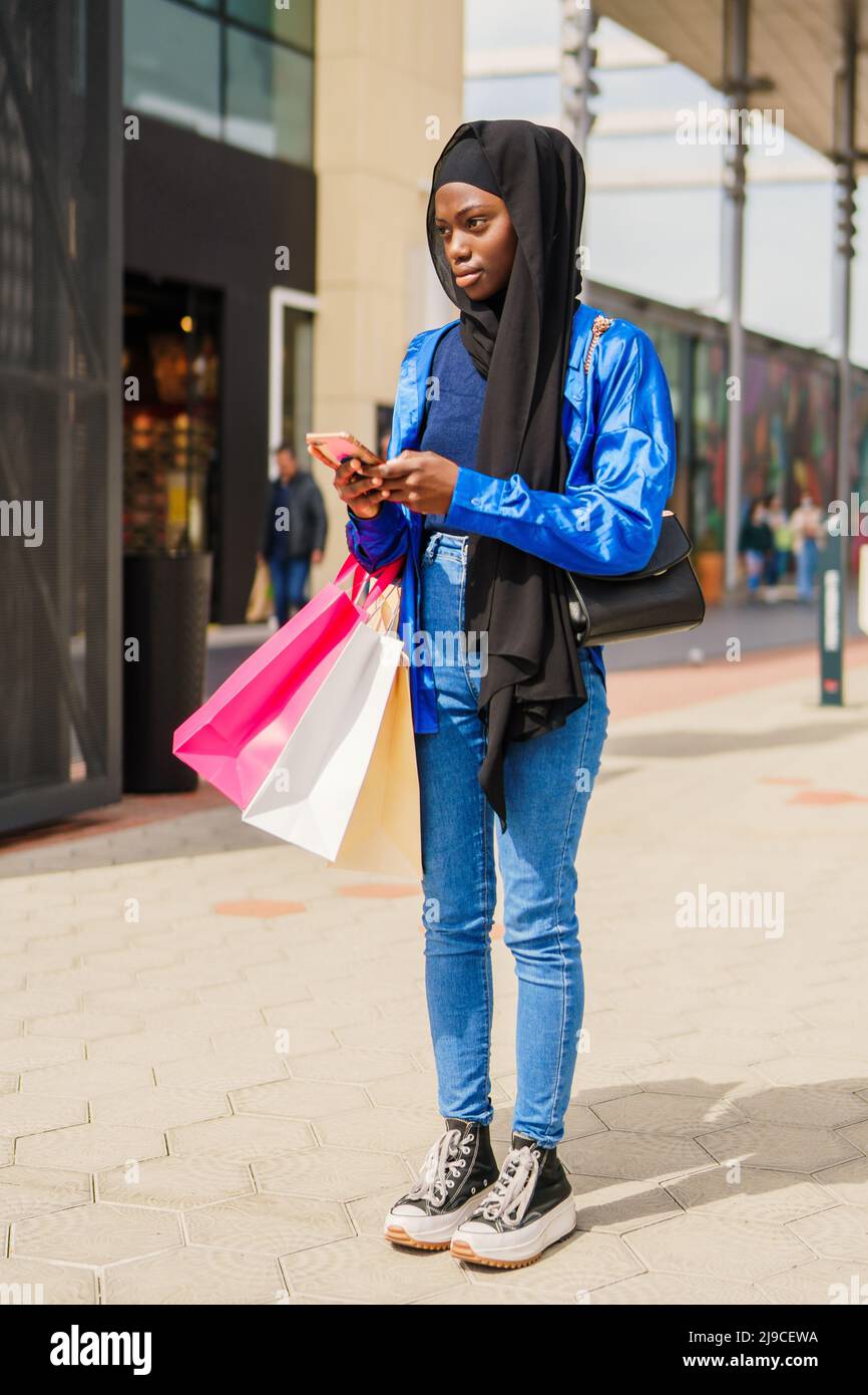 Stylish Muslim shopaholic texting outside mall Stock Photo