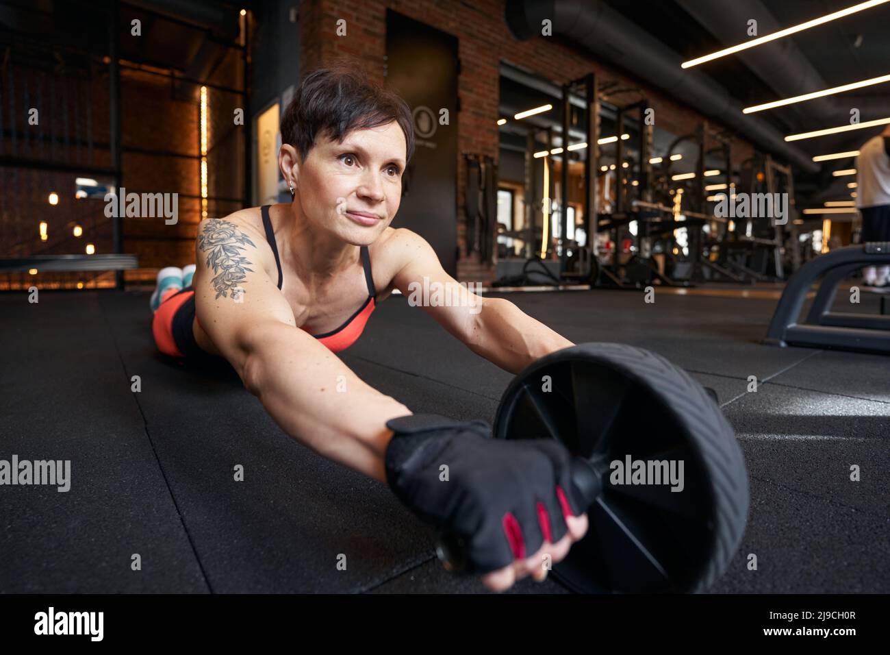 Sportswoman doing ab wheel rollout on gym floor Stock Photo - Alamy