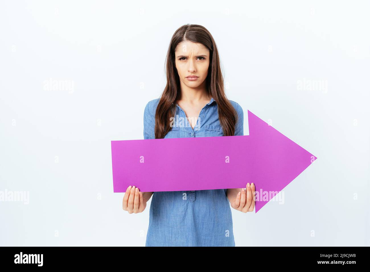 Angry displeased young woman holding big arrow pointing to the side ...