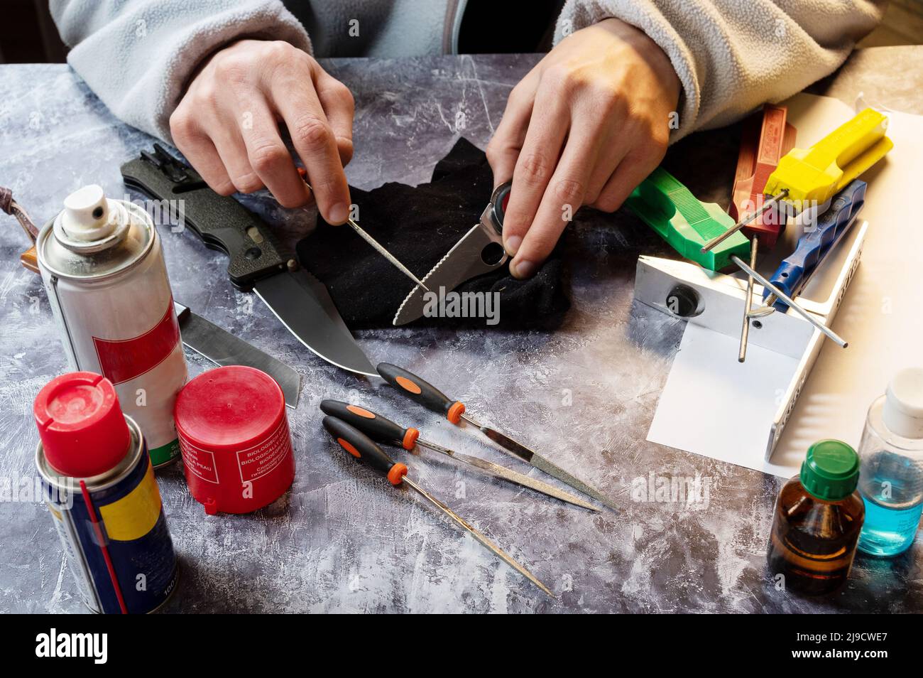 Sharpen the serrated knife. Sharpen a knife with a saw. Tool in hand. Oil, grindstones and tools on the table. Stock Photo
