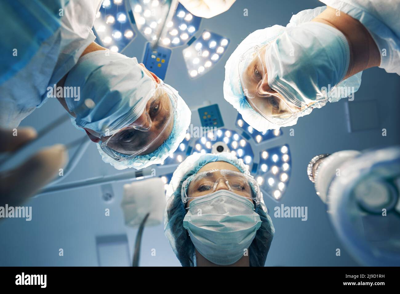 Three doctors bending over patient during laparoscopic operation Stock
