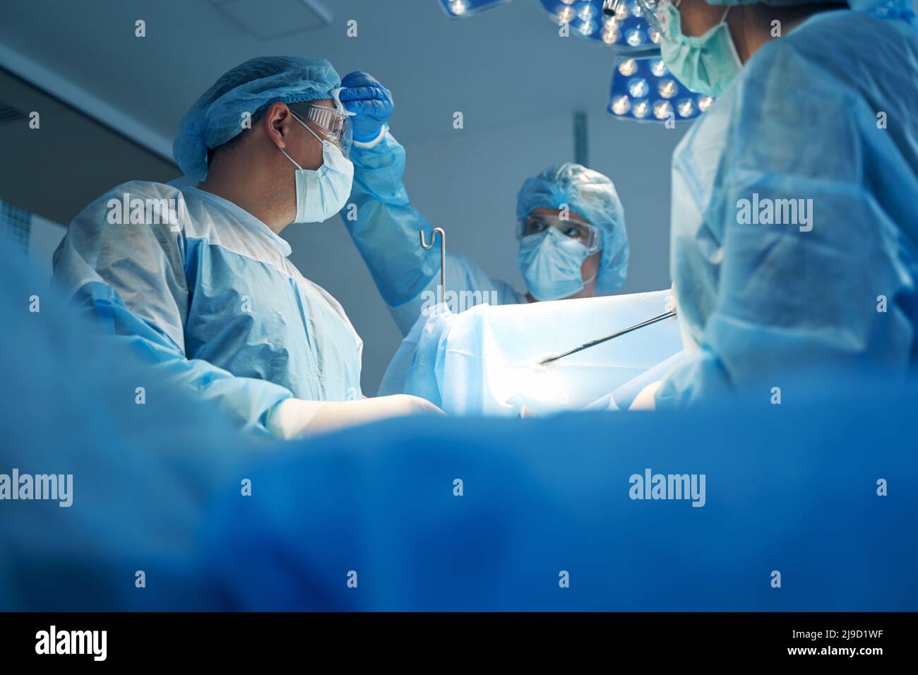 Nurse wiping sweat from surgeon forehead during operation Stock Photo