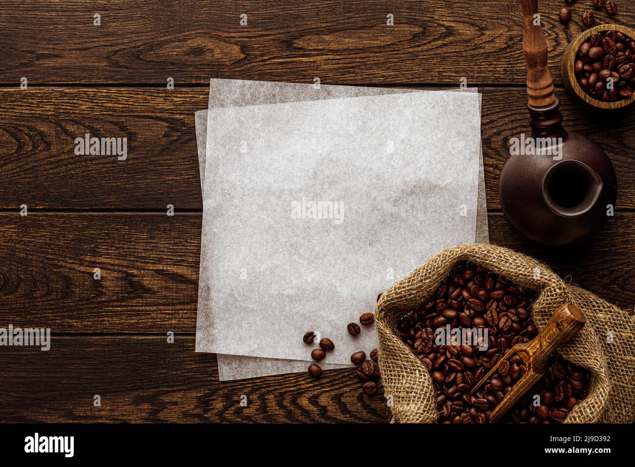 Freshly roasted coffee beans. Wooden background with hot aromatic drink preparation accessories and packing craft paper sheets. Turkish cezve pot, woo Stock Photo