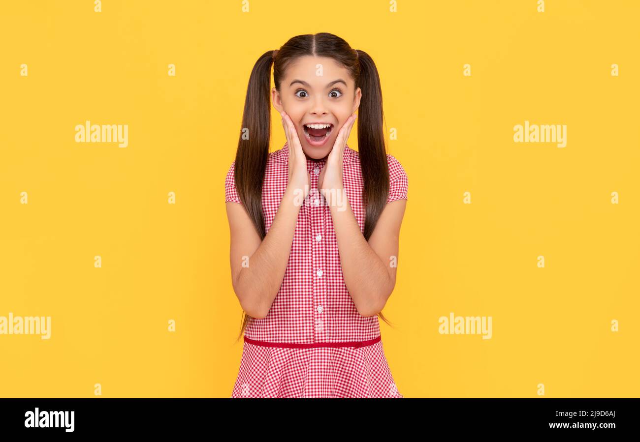 Shocked eye-popping tween girl show surprise yellow background, OMG Stock Photo