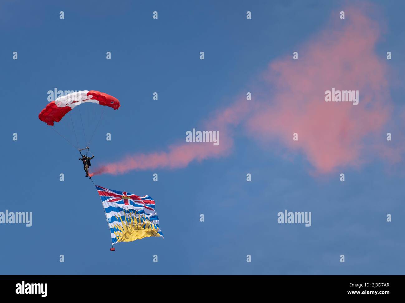 A member of the Canadian Armed Forces Parachute Team, The Skyhawks, trails red smoke and the flag of British Columbia above Victoria on May 22, 2022. Stock Photo