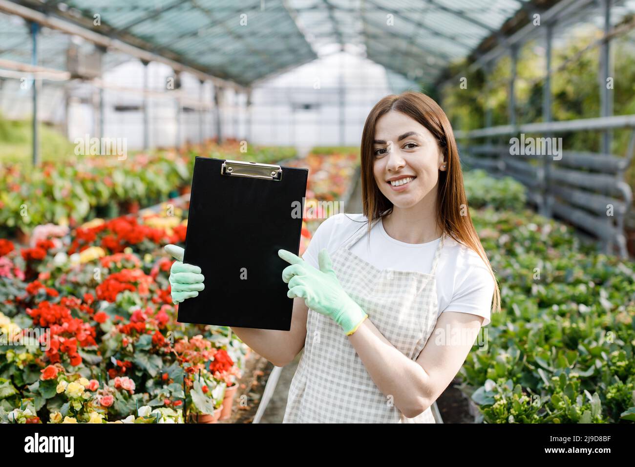 Portrait of gardener woman at work in greenhouse with notebook examines ...