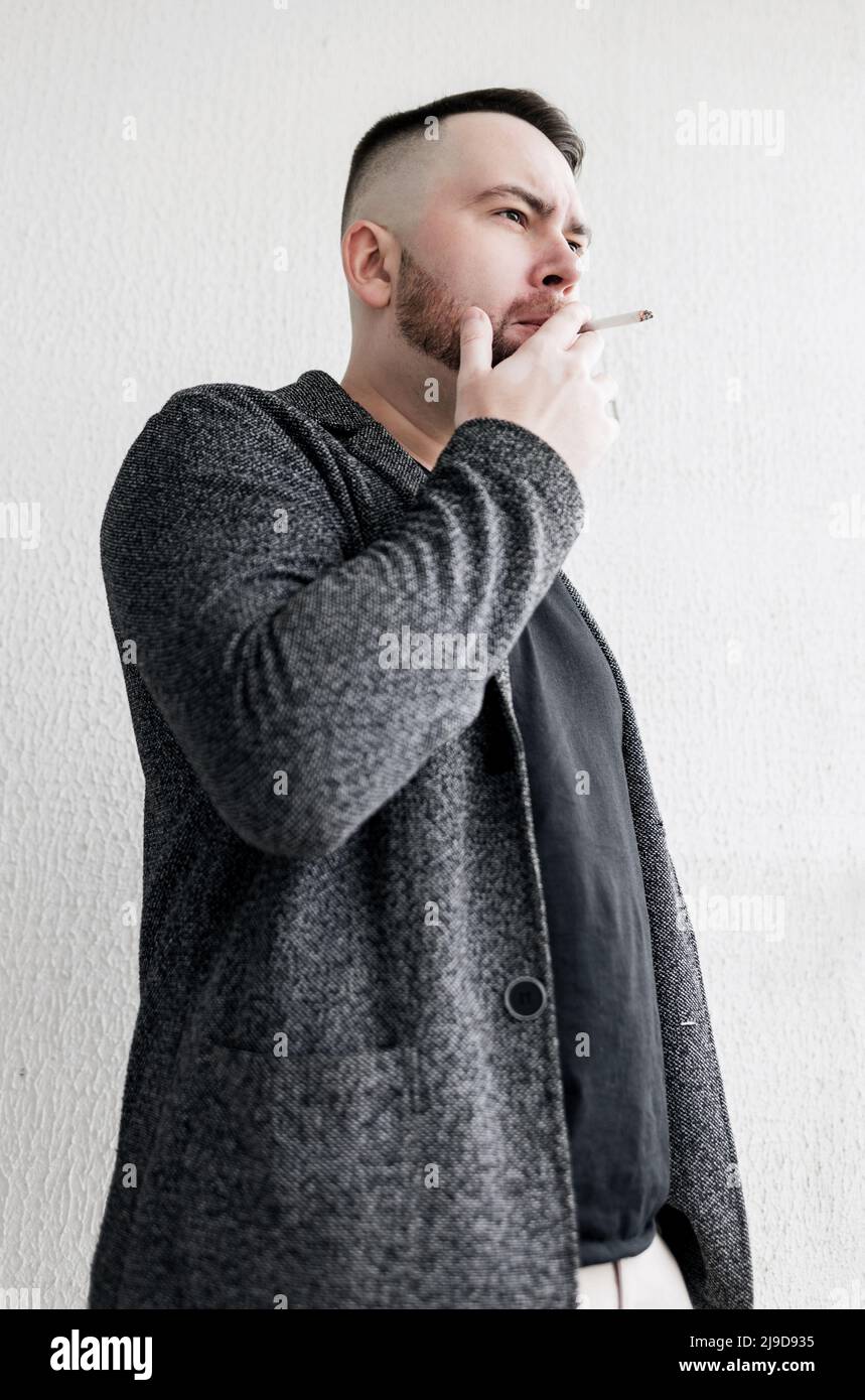 Young bearded man smoking cigarette. Guy addicted nicotine of cigarettes .  He smoke cigarette in public at outdoor Stock Photo