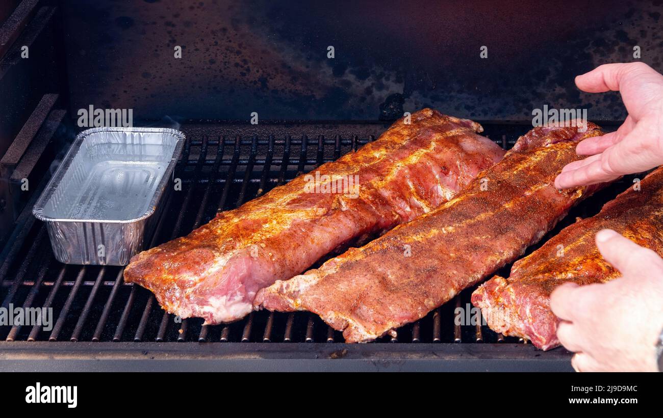 Armature cook adds a rack of baby back ribs to a smoker Stock Photo Alamy