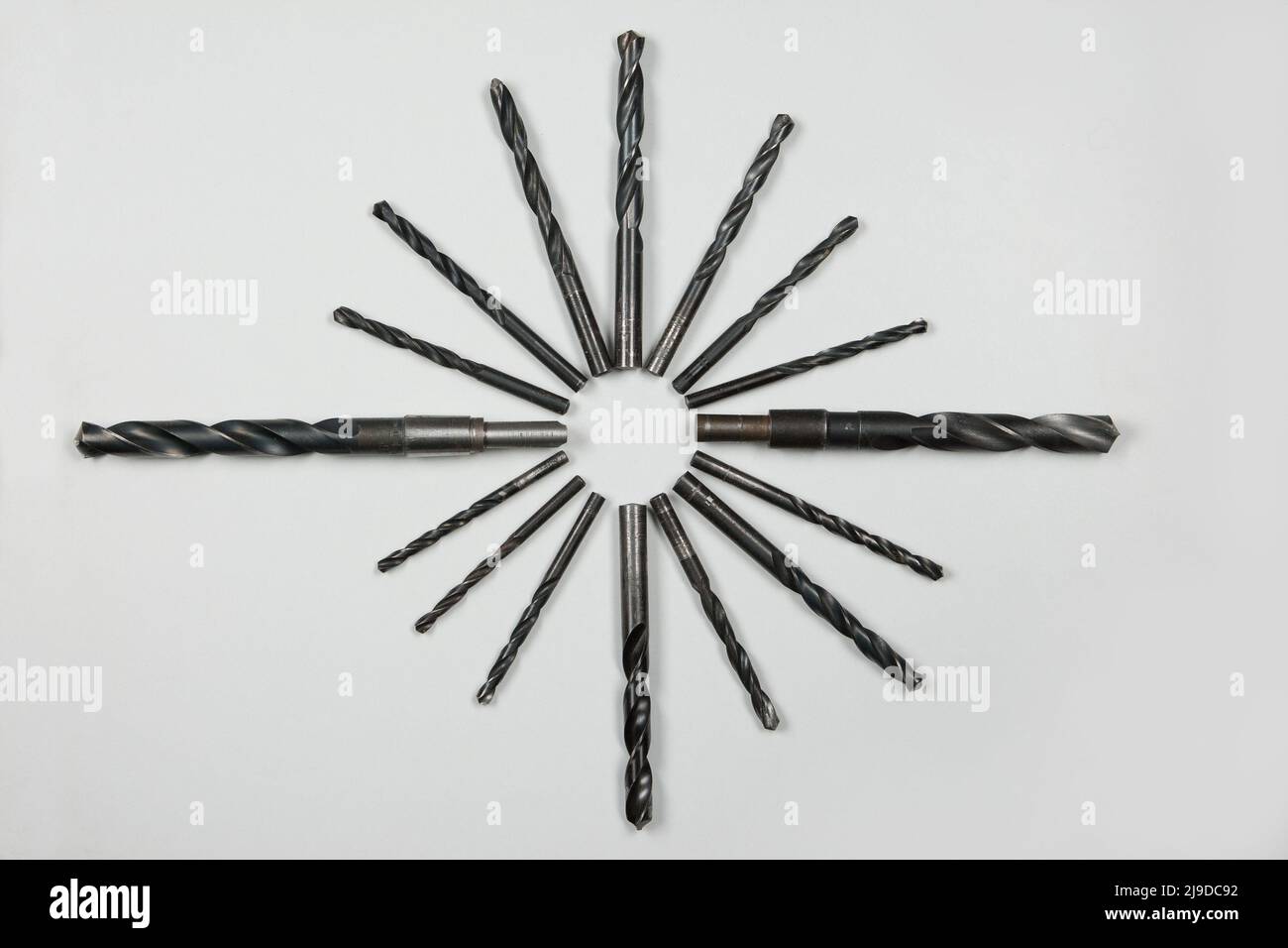 Various used twist drills are arranged to a star on a white background. In 1863 Giovanni Martignoni designed the first drill with a twisted groove. Stock Photo