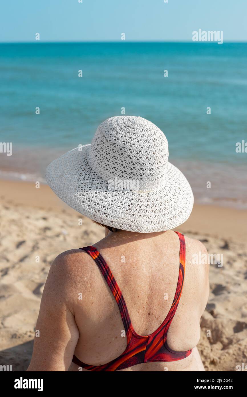 Elderly woman in a swimsuit and a white hat on the beach. Summer ...