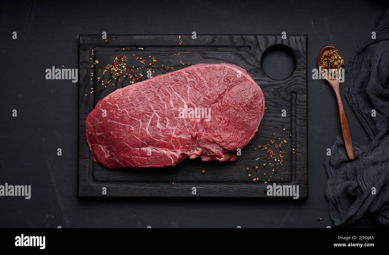 Raw beef tenderloin lies on a wooden cutting board on a black table