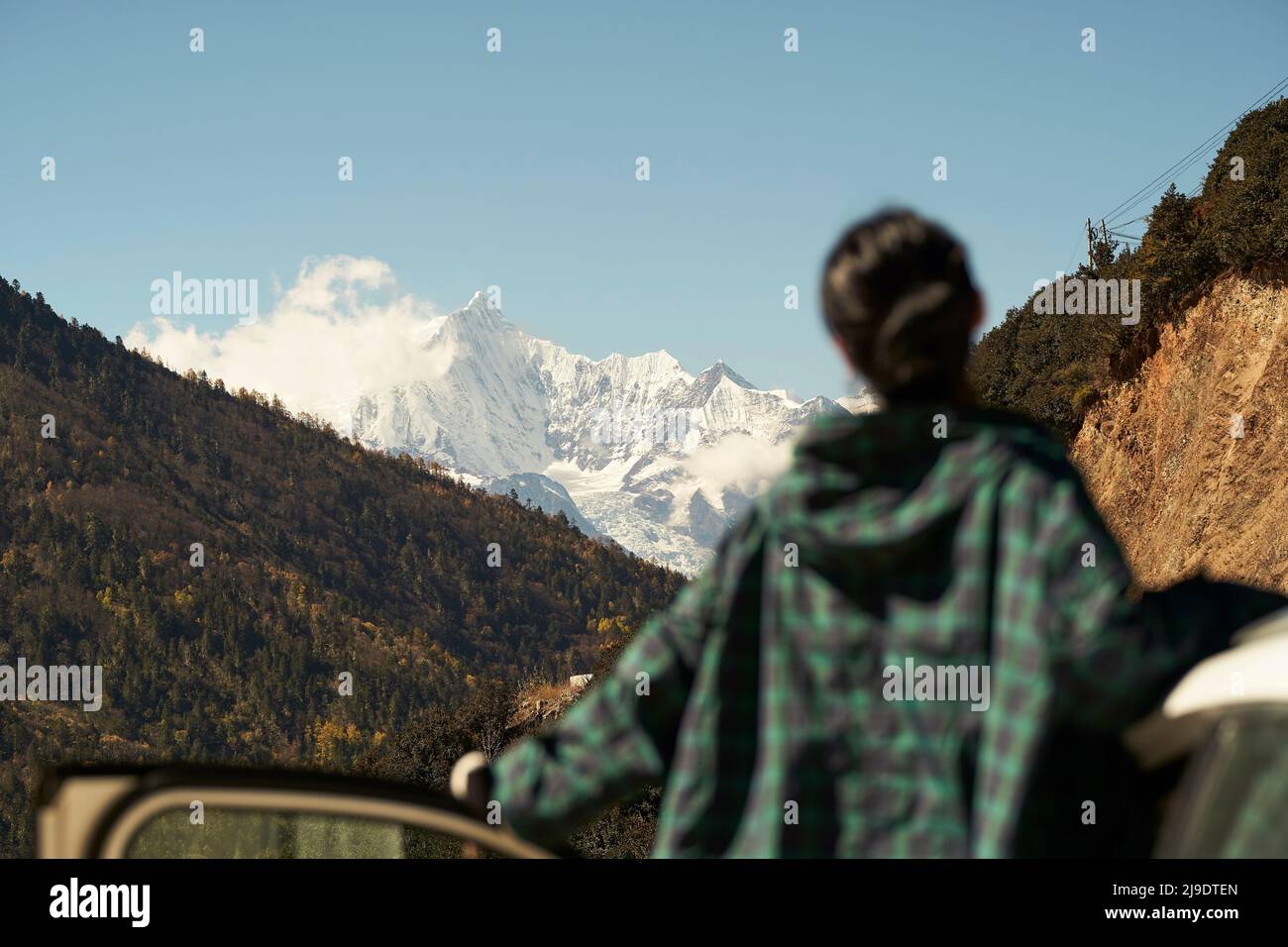 rear view of asian woman female tourist looking at snow covered mount kawaboge in yunnan, china, focus on background Stock Photo