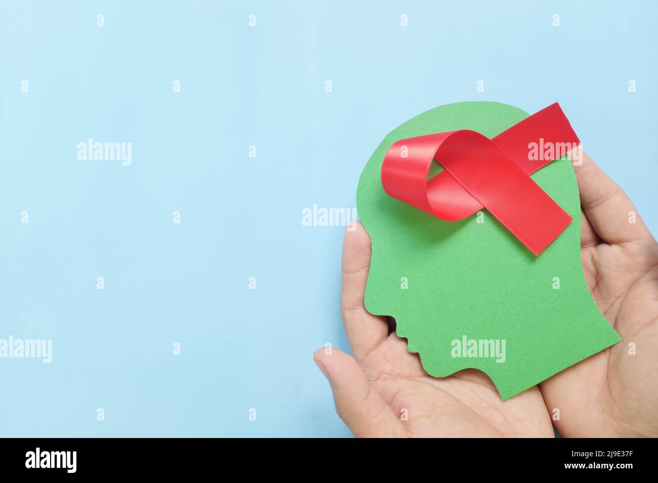 Hand holding human head profile with red awareness ribbon on brain