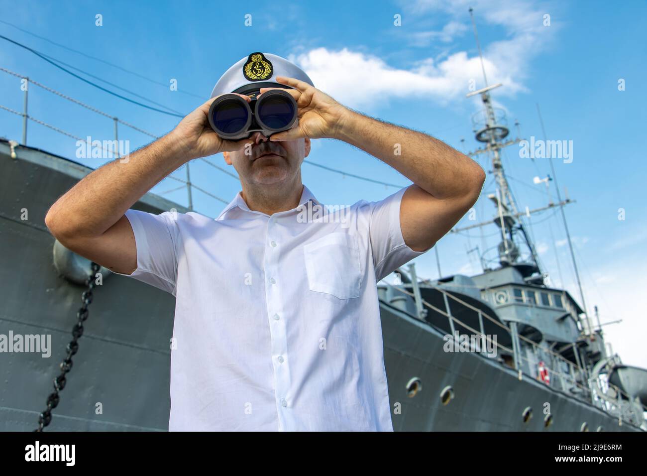 Navy officer standing beside warship and looking around with binocular. Stock Photo