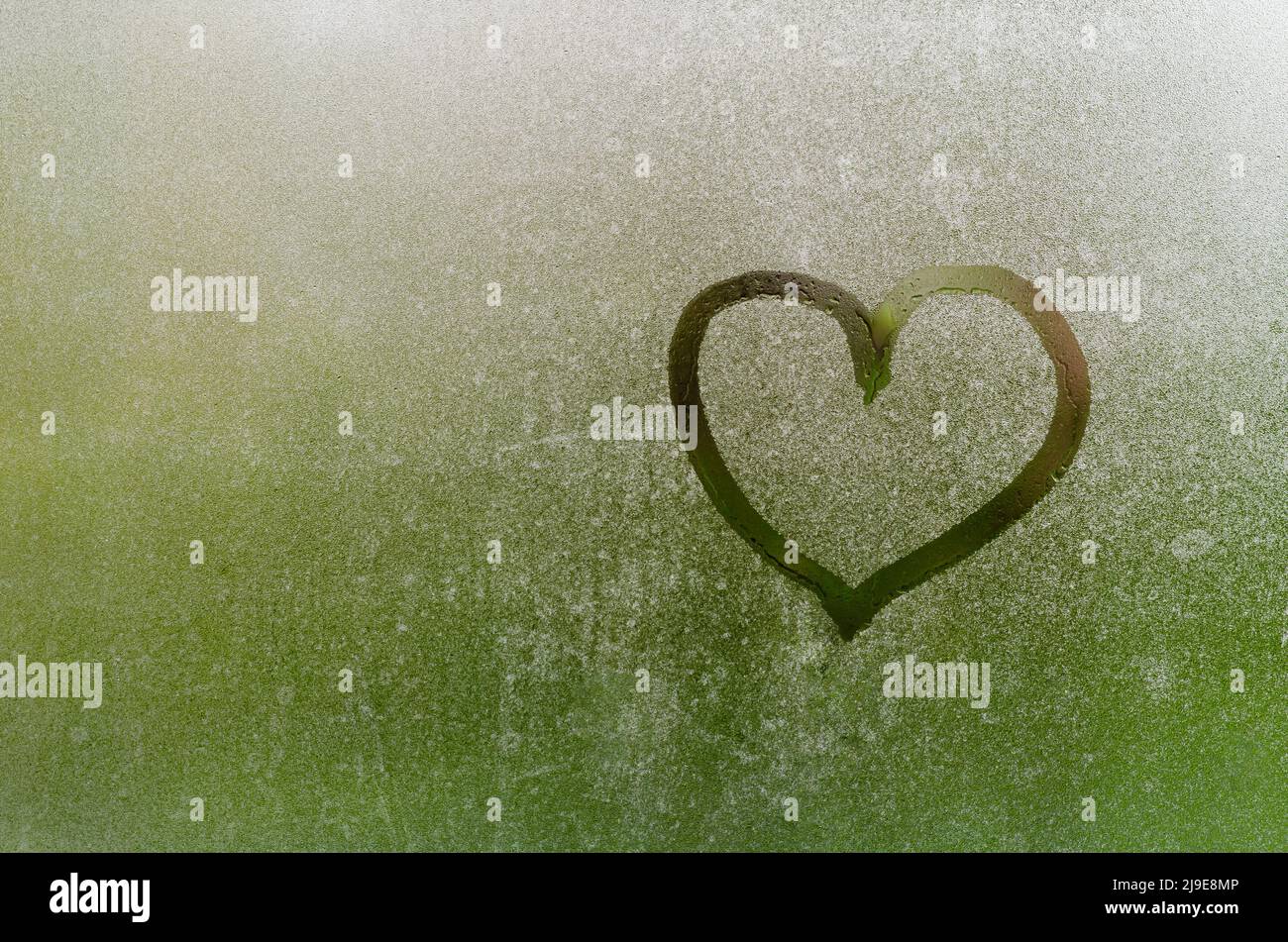 Heart painted on window which fogged up after rain with blurred green color background. Stock Photo