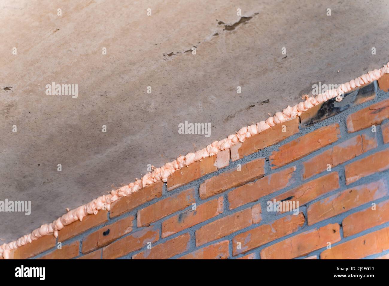 The gap between the concrete floor panels and the brick wall is filled with mounting foam at a
