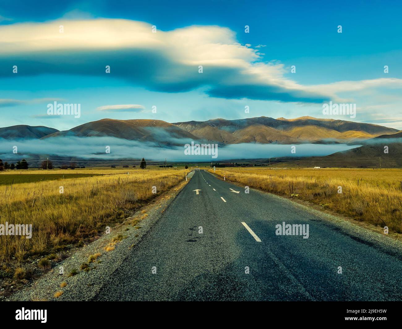 The asphalt road heading to  the fluffy cloud both above and below the hills Stock Photo