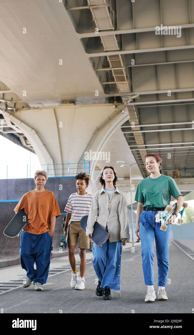 Full length shot of diverse group of teenagers in skatepark outdoors at urban area wearing sporty outfits Stock Photo