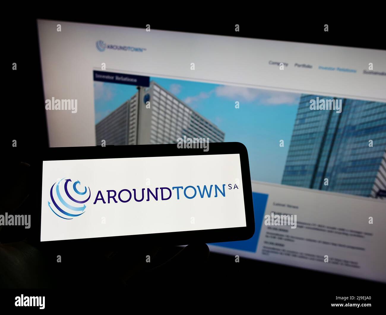 Person holding cellphone with logo of real estate company Aroundtown SA on screen in front of business webpage. Focus on phone display. Stock Photo
