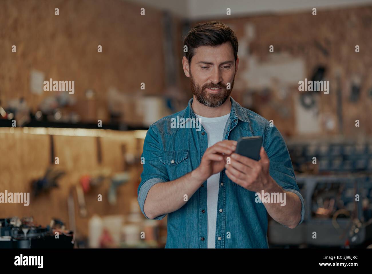 Male worker using phone standing in own workshop Stock Photo