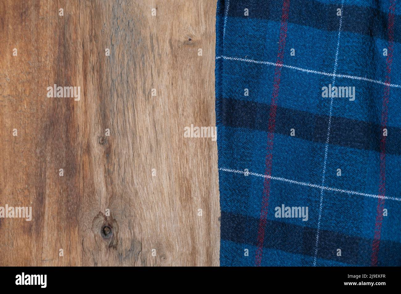 The blue checkered fabric lies against the wooden background. A towel or kitchen napkin on the rough boards or kitchen table. Stock Photo