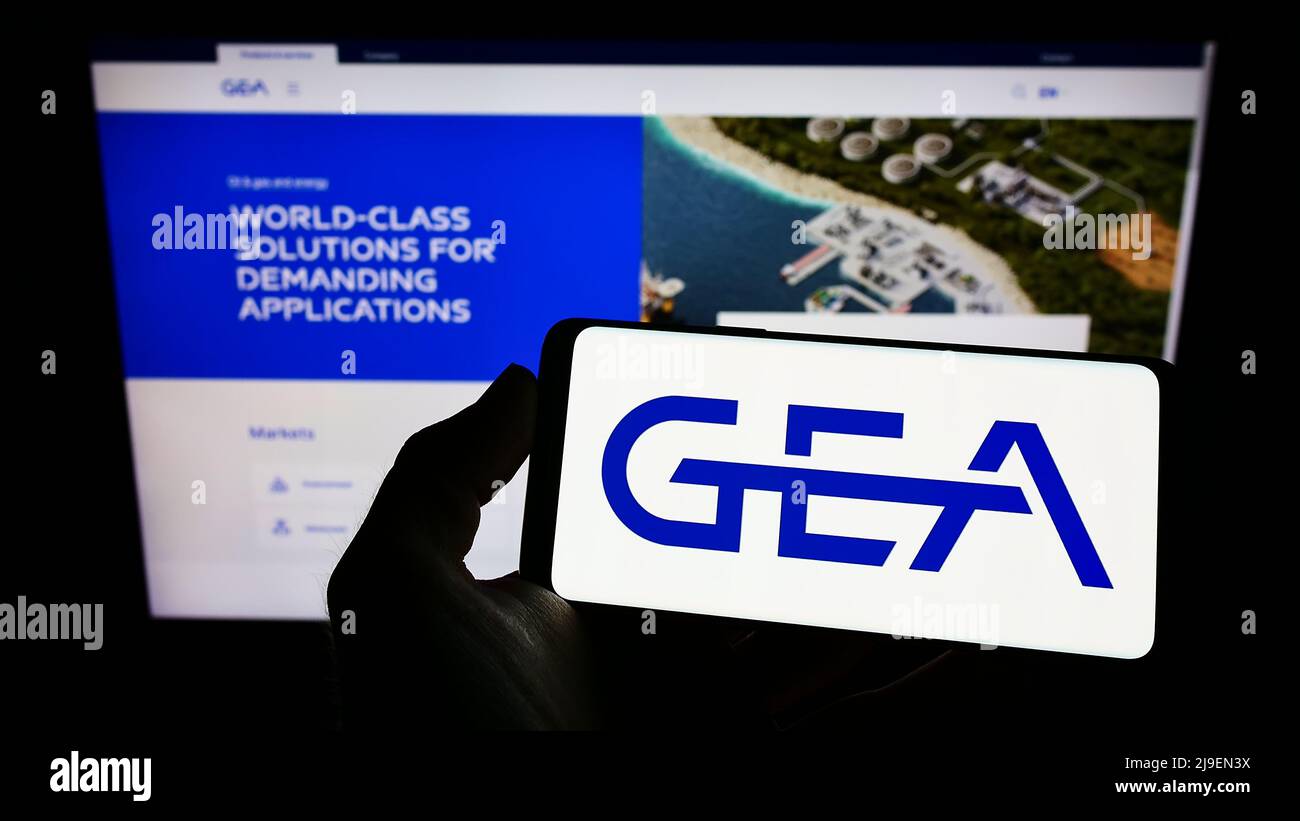 Person holding smartphone with logo of German food processing company GEA Group AG on screen in front of website. Focus on phone display. Stock Photo