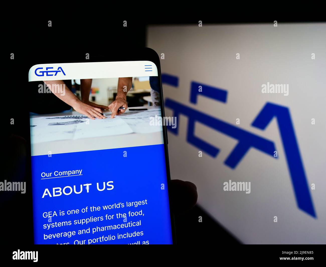 Person holding mobile phone with website of German food processing company GEA Group AG on screen with logo. Focus on center of phone display. Stock Photo