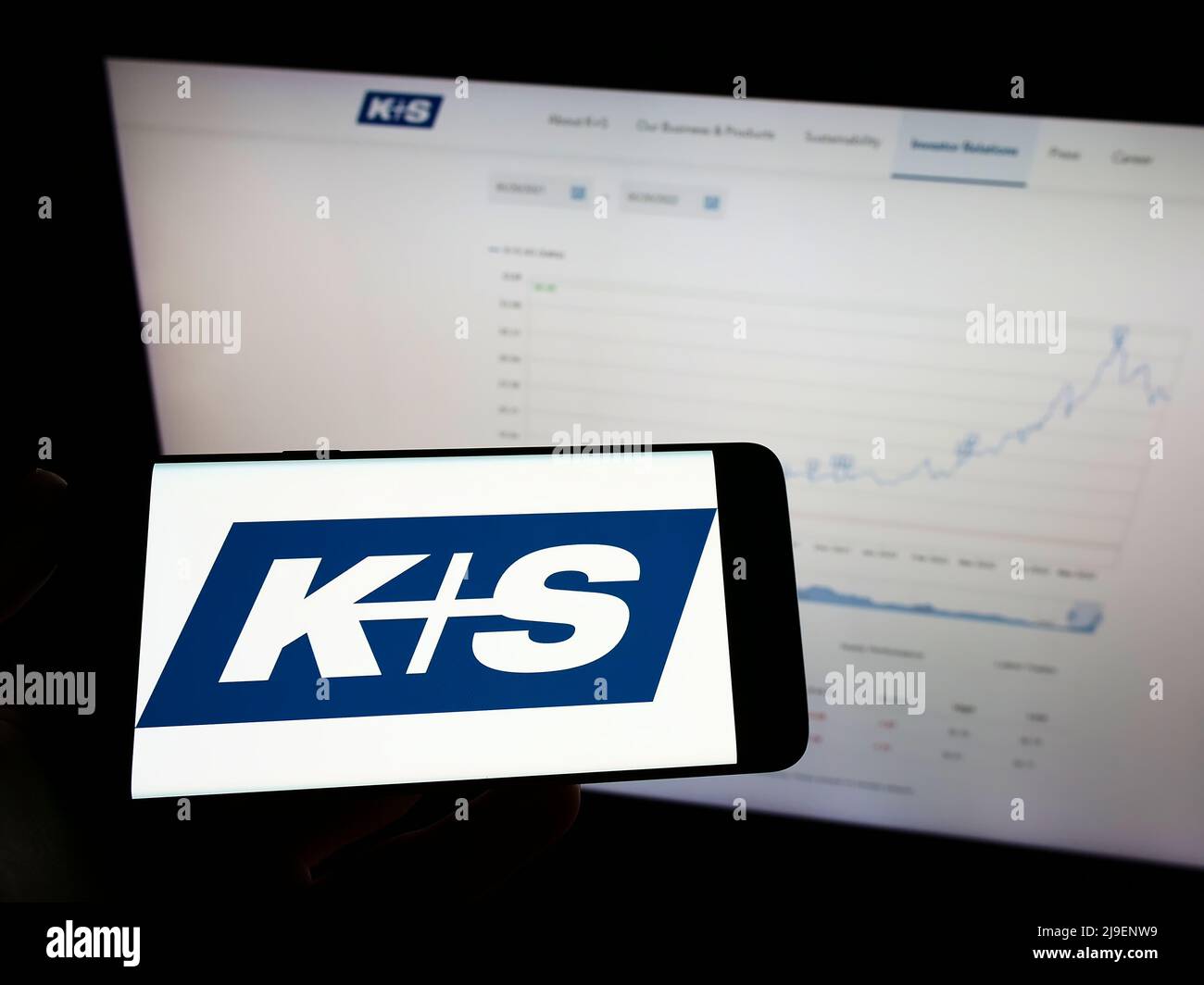 Person holding mobile phone with logo of German mining company KS AG (K plus S) on screen in front of business web page. Focus on phone display. Stock Photo