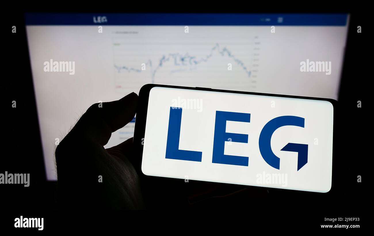 Person holding mobile phone with logo of German real estate company LEG Immobilien SE on screen in front of web page. Focus on phone display. Stock Photo