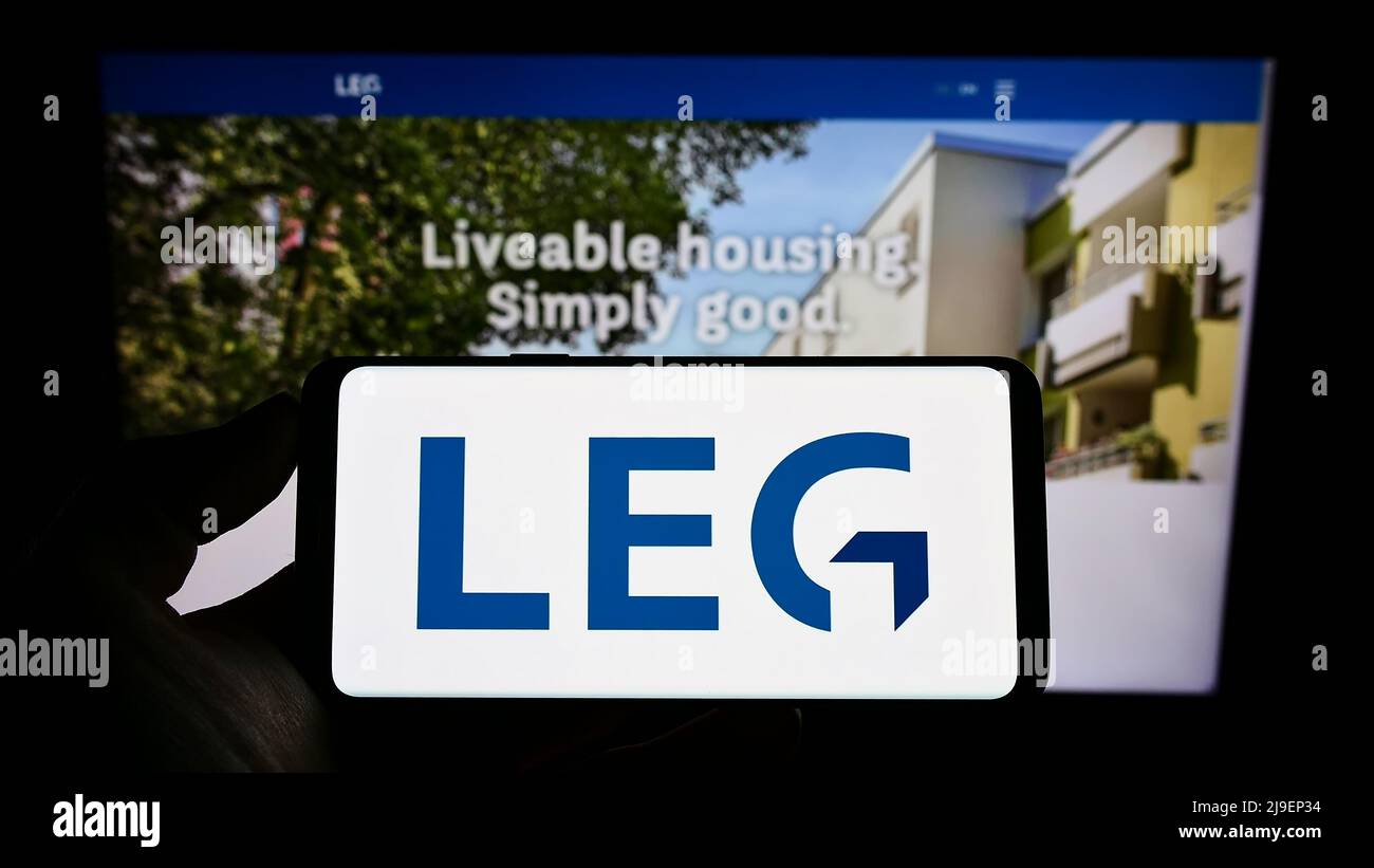 Person holding cellphone with logo of German real estate company LEG Immobilien SE on screen in front of business webpage. Focus on phone display. Stock Photo